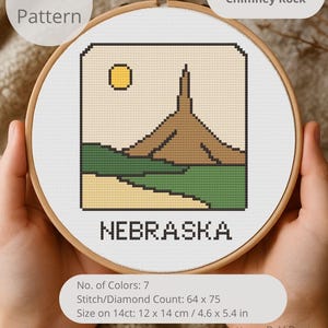 May include: A cross-stitch pattern of Nebraska's Chimney Rock, featuring a tan landscape with a brown rock formation and a yellow sun. The word "NEBRASKA" is stitched below. The pattern is 4.6 x 5.4 inches and uses 7 colors.