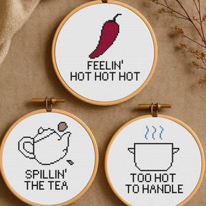 May include: Three round embroidery hoops with cross-stitch designs. One features a red chili pepper with the text "FEELIN' HOT HOT HOT." Another shows a teapot with "SPILLIN' THE TEA." The last has a pot with steam and "TOO HOT TO HANDLE."