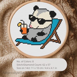 May include: Cross-stitch embroidery in a wooden hoop features a pixelated opossum wearing sunglasses and relaxing in a blue beach chair, holding a drink. The design includes the text "No. of Colors: 8", "Stitch/Diamond Count: 62 x 57", and "Size on 14ct: 4.4 x 4.1 in".