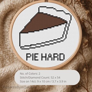 Könnte beinhalten: Kreuzstich-Stickerei in einem Holzrahmen. Das Design zeigt ein Stück Kuchen in Braun und Weiß, umrandet in Schwarz, mit den Worten "PIE HARD" darunter. Die Größe beträgt 9 x 10 cm.