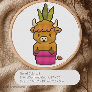 May include: A cross-stitch embroidery in a wooden hoop features a cartoon bull with a pineapple head and a pink pot. The design includes 8 colors and measures 2.6 x 5 inches. The text "PatternsByViDesigns" is at the bottom.
