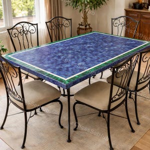 May include: A rectangular dining table with a mosaic blue top, framed by a green and white border. The table is supported by black metal legs and surrounded by six matching chairs with beige upholstered seats and ornate black metal backs.