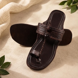 May include: A pair of dark brown leather sandals featuring a toe loop, a braided strap connecting the toe loop to the main horizontal band, and decorative stitching along the edges of the straps and the sole of the footwear.
