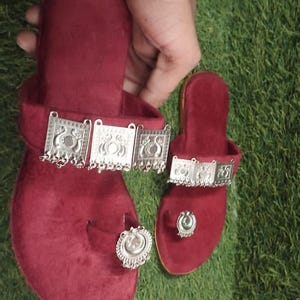 May include: Burgundy velvet sandals with silver-toned embellishments. The sandals feature a toe ring and decorative straps with dangling charms. One adult-sized sandal and one smaller sandal are visible.