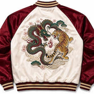 Puede incluir: Una chaqueta bomber de satén con un panel trasero de color crema que presenta un gran bordado detallado de un dragón verde y un tigre frente a frente, rodeados de flores de cerezo y nubes. Las mangas y el cuello son de color burdeos a rayas.