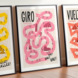 Set of three Grand Tour cycling posters—Giro, Tour, and Vuelta, focussing on the Giro design in the centre and with the Tour and Vuelta designs shown cropped on either side. The print is framed and leaning against a wall and features fun illustrations of a pink race route on a neutral background, including riders, spectators and famous Italian landmarks.