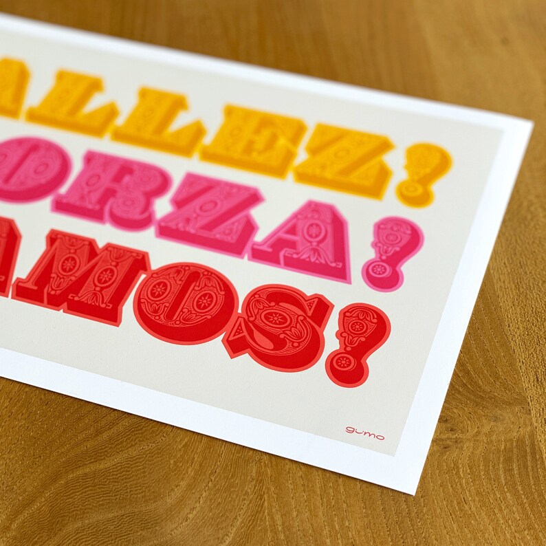 Op de afbeelding: Een rechthoekige kunstdruk op een lichtgrijze achtergrond met drie regels tekst in een vetgedrukt 3D-lettertype. De bovenste regel toont ALLEZ! in geel, de middelste FORZA! in roze en de onderste VAMOS! in rood. Het woord gumo staat in de hoek.