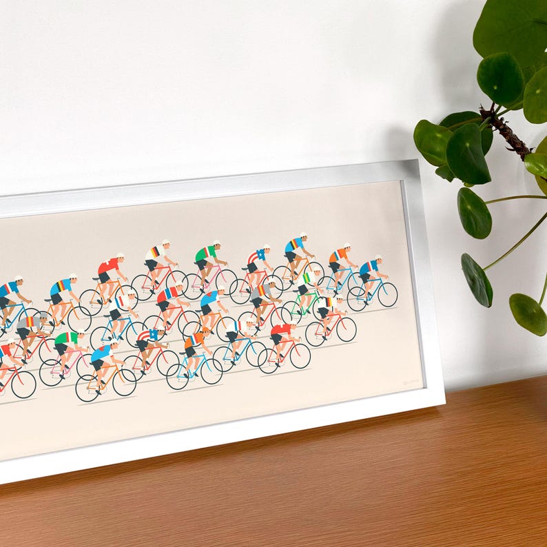Op de afbeelding: Een ingelijste horizontale print met een gestileerde illustratie van een grote groep wielrenners in kleurrijke truien op fietsen. Het kunstwerk is geplaatst tegen een lichtbeige achtergrond en toont een peloton renners in diverse posities.
