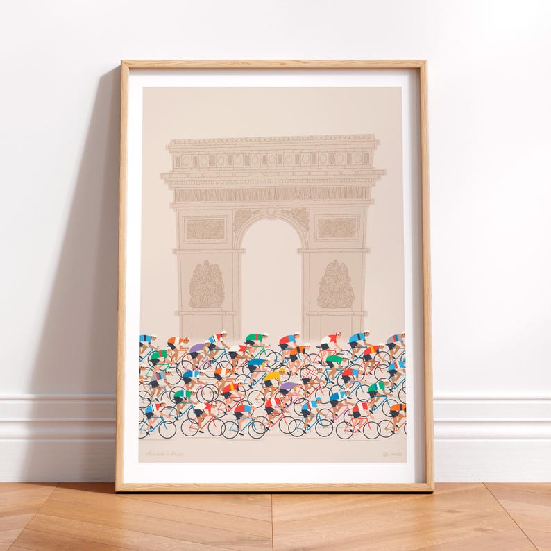 This photo of a contemporary cycling art print in ecru, features a colourful peloton riding past the Arc de Triomphe in Paris. The print is framed in a simple oak frame and is sat on a wooden herringbone style floor and leaning against a white wall.
