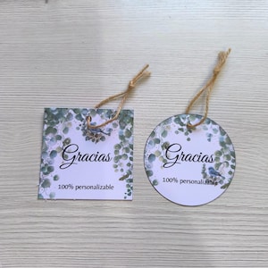 Puede incluir: Dos etiquetas con hilo, una cuadrada y otra redonda, presentan la palabra "Gracias" en cursiva. Ambas etiquetas tienen un diseño de eucalipto en acuarela y un pequeño pájaro azul. También se incluye el texto "100% personalizable".