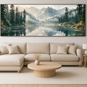 May include: A panoramic landscape wall art print featuring a serene lake reflecting towering snow-capped mountains and a dense forest of evergreen trees shrouded in morning mist. The scene displays cool blue and green tones with soft natural lighting.
