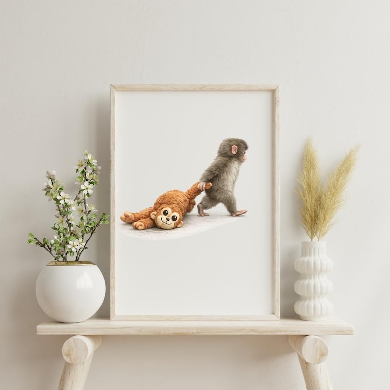 May include: A framed print showing a grey monkey pulling a brown stuffed monkey. The stuffed toy has a smiling face. The print is displayed on a white background, with a white vase and flowers on a wooden shelf.