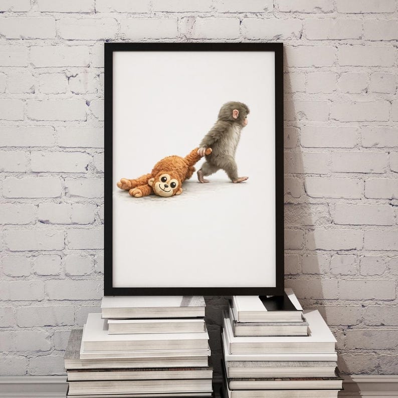 May include: A framed print showing a grey baby monkey walking and pulling a brown stuffed monkey. The artwork is displayed on a stack of books against a white brick wall. The image has a playful and whimsical theme.