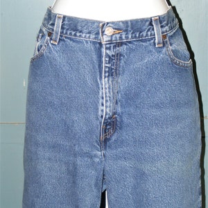 May include: Close-up of blue denim jeans. The jeans have a button closure, belt loops, and pockets. The denim is a medium wash with visible stitching details. The jeans are displayed on a mannequin.