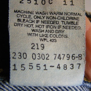 May include: A close-up of a white clothing tag with black text. The tag includes care instructions: machine wash warm, non-chlorine bleach if needed, tumble dry hot, and hot iron if needed. The tag also has several numerical codes.