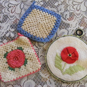 May include: Three handmade crochet pot holders. One is square with a blue border, another is square with a pink rose, and the third is round with a red flower and green leaves. The pot holders are cream-colored.