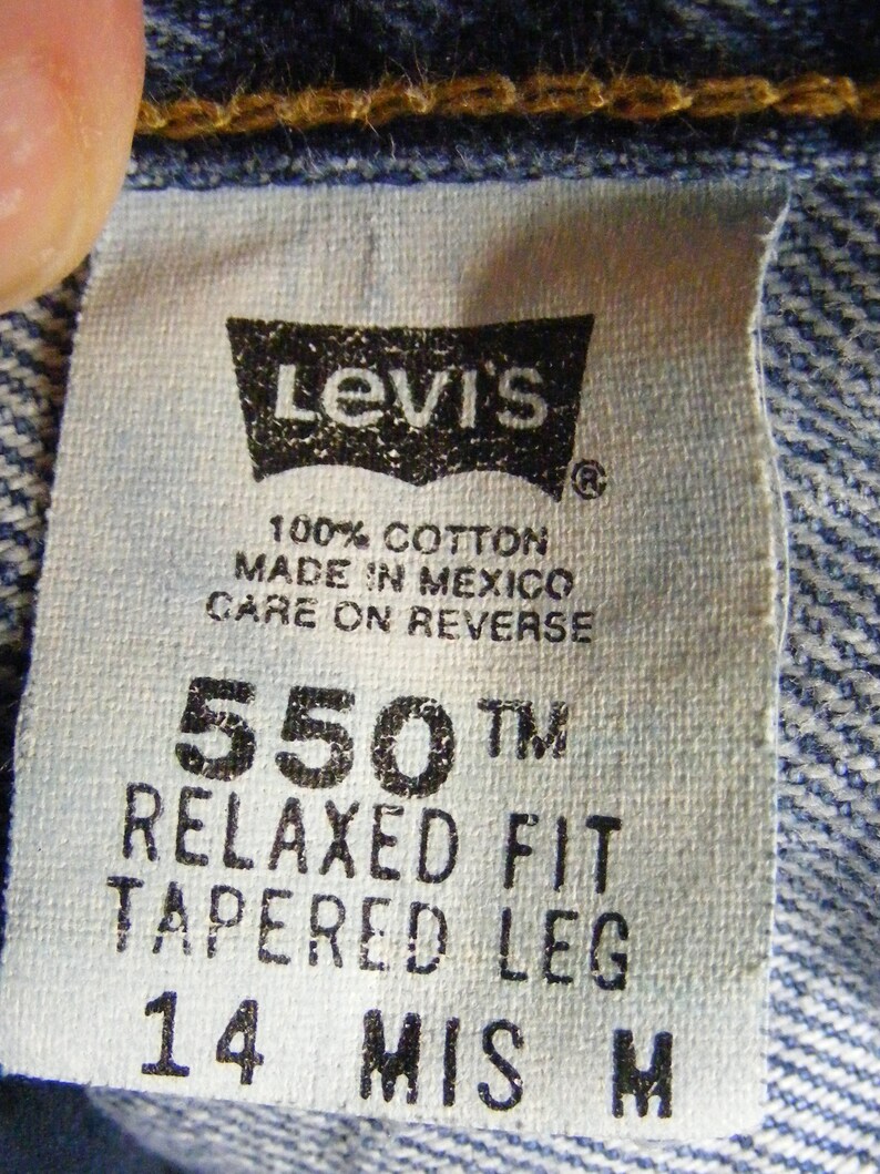 May include: Close-up of a Levi's tag on denim fabric. The tag is white with black text, including "Levi's", "550 Relaxed Fit Tapered Leg", and "100% Cotton Made in Mexico". The tag is stitched to the blue denim.