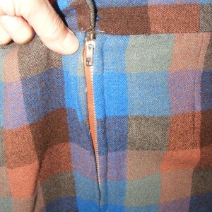 May include: A close-up of a brown, blue, and orange plaid fabric with a zipper running down the center.
