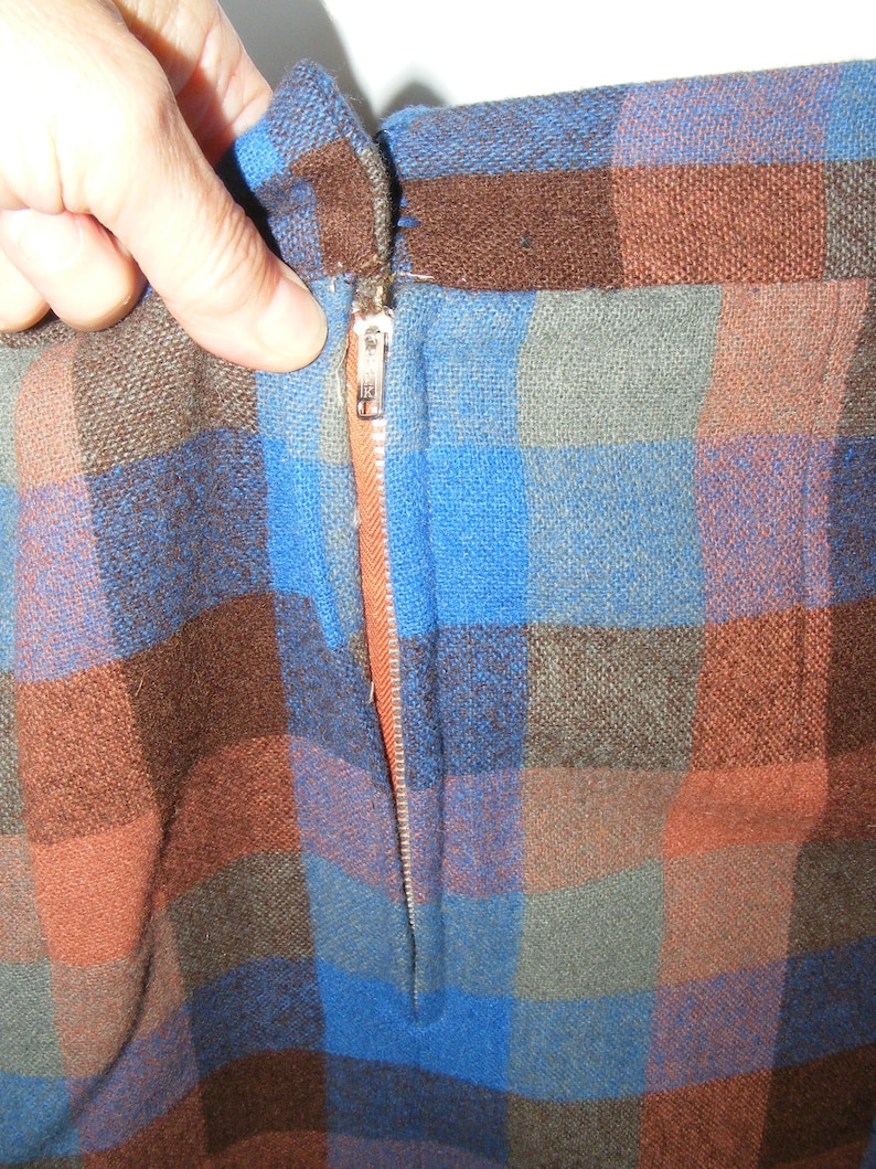 May include: A close-up of a brown, blue, and orange plaid fabric with a zipper running down the center.
