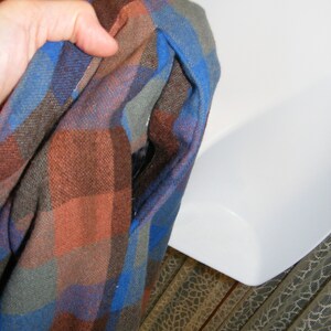 May include: A blue, brown, and gray plaid flannel shirt with a hole in the fabric.