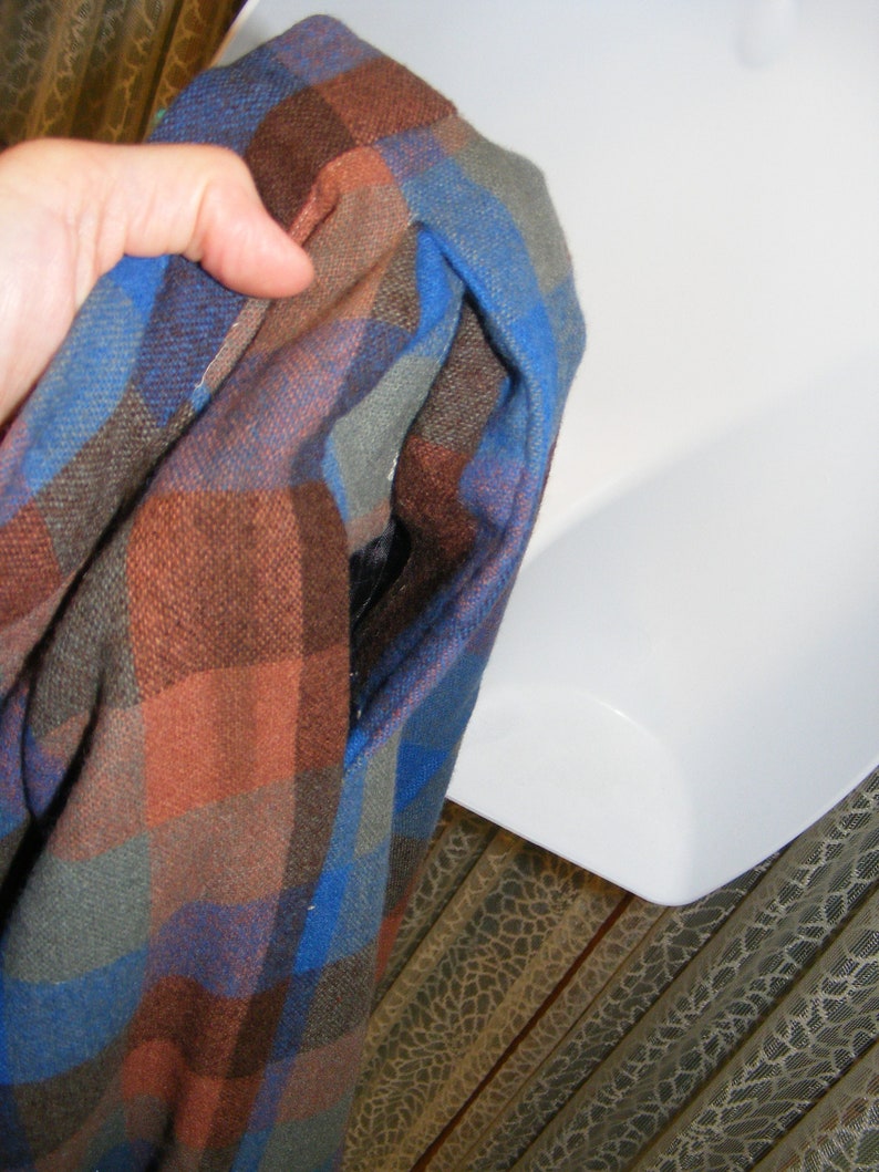 May include: A blue, brown, and gray plaid flannel shirt with a hole in the fabric.