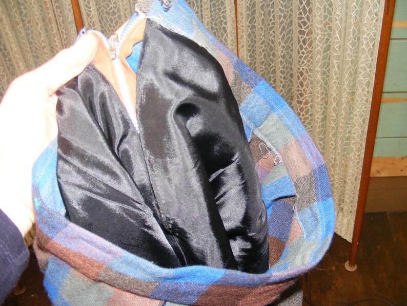 May include: A blue and brown plaid jacket with a black satin lining. The jacket is unzipped and the lining is folded over.