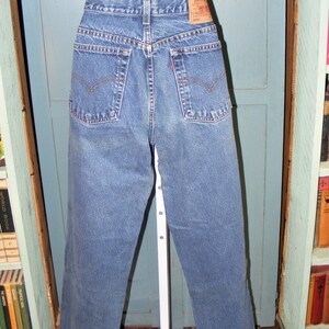 May include: Blue denim jeans with a classic five-pocket design. The jeans have a straight leg cut and a faded wash. A red Levi's tag is visible on the back pocket. The jeans are displayed on a white mannequin.