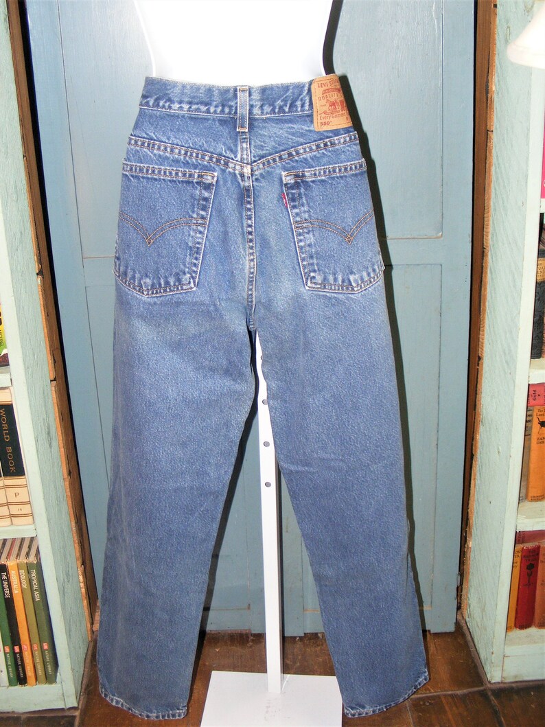May include: Blue denim jeans with a classic five-pocket design. The jeans have a straight leg cut and a faded wash. A red Levi's tag is visible on the back pocket. The jeans are displayed on a white mannequin.