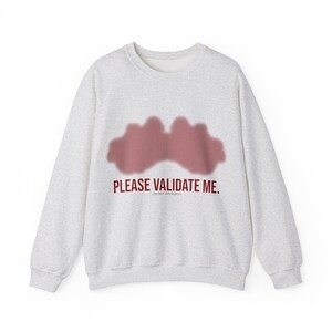 May include: A light gray sweatshirt with a crew neck. The sweatshirt features a maroon-colored abstract design and the text "PLEASE VALIDATE ME. DO NOT APPROACH" in maroon lettering.
