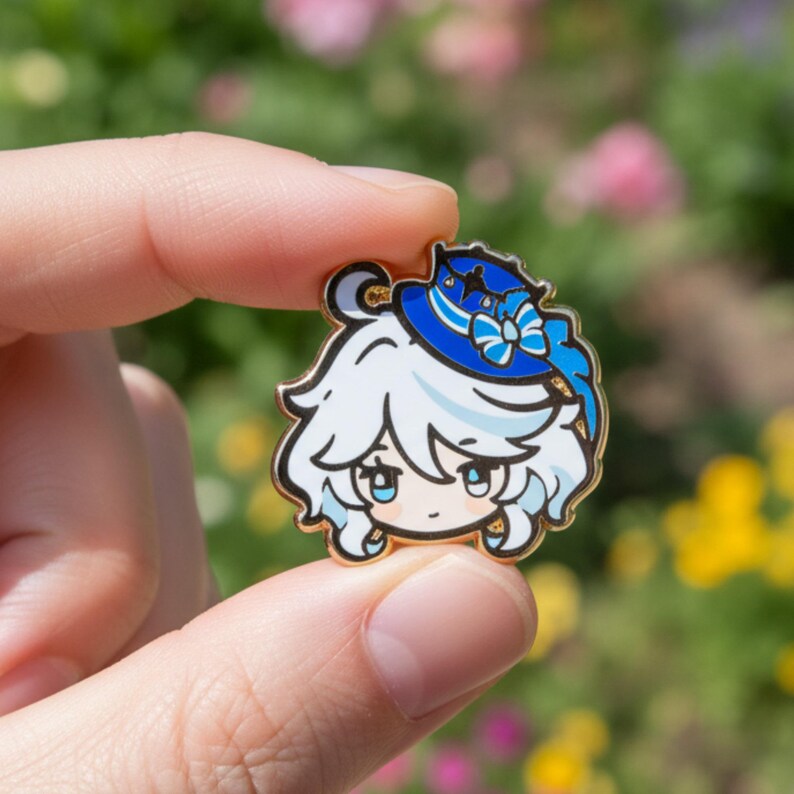 Peut inclure: &Eacute;pingle en &eacute;mail de couleur or repr&eacute;sentant un personnage de dessin anim&eacute; aux cheveux blancs et un chapeau bleu avec un n&oelig;ud. Le personnage a les yeux bleu clair et une expression souriante. L'&eacute;pingle est tenue entre deux doigts.