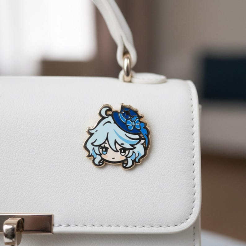Peut inclure: Une &eacute;pingle en &eacute;mail de couleur or repr&eacute;sentant un personnage de dessin anim&eacute; aux cheveux bleu clair et un chapeau bleu avec un n&oelig;ud. L'&eacute;pingle est attach&eacute;e &agrave; un sac &agrave; main blanc. Le personnage a de grands yeux et un petit sourire.