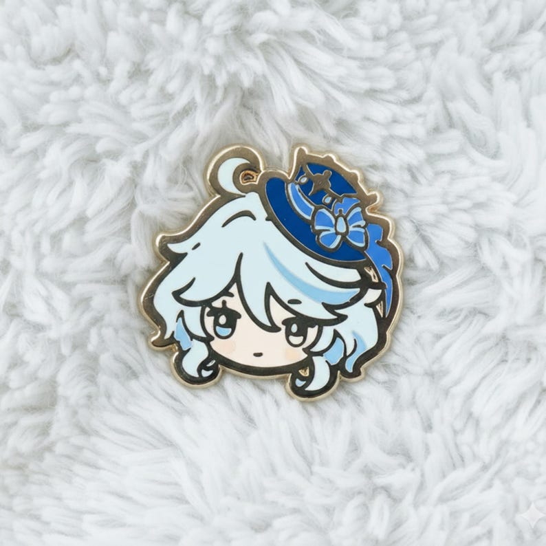 Peut inclure: &Eacute;pingle en &eacute;mail de couleur or repr&eacute;sentant un personnage de dessin anim&eacute; aux cheveux bleu clair et un chapeau bleu avec un n&oelig;ud. Le personnage a de grands yeux et une petite bouche. L'&eacute;pingle est pos&eacute;e sur un fond blanc et duveteux.