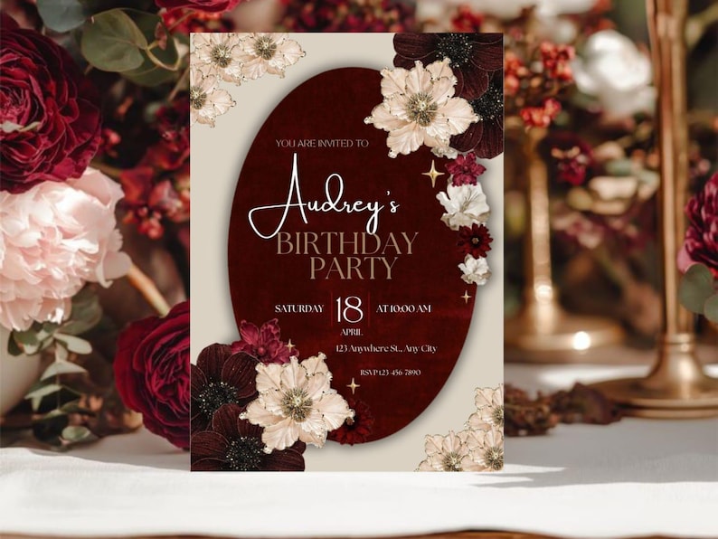 May include: A birthday party invitation with a burgundy oval in the center, adorned with floral accents. The invitation reads "Audrey's Birthday Party" with the date, time, and location details. The design features a cream background and elegant script.