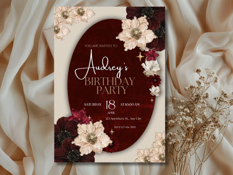 May include: A birthday party invitation with a burgundy oval in the center, adorned with floral accents. The invitation reads "Audrey's Birthday Party" with the date, time, and location details. The design features cream and burgundy colors.