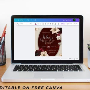 May include: A laptop displays a birthday party invitation design. The invitation features a burgundy oval with floral accents and the text "Audrey's Birthday Party." The laptop is on a wooden desk with office supplies.