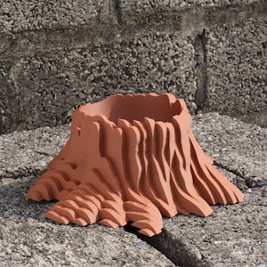May include: A terracotta-colored planter shaped like a tree stump. The planter has a textured, layered design with a wide opening at the top. The planter is made of a solid material and is suitable for indoor or outdoor use.