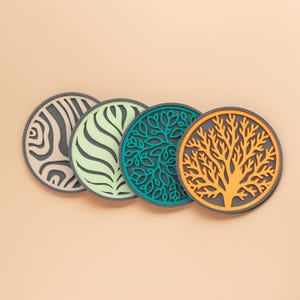 May include: Four round coasters with decorative designs. The coasters feature a zebra stripe pattern, a wavy pattern, a leafy design, and a tree design. The coasters have a gray border and are in shades of gray, green, teal, and orange.