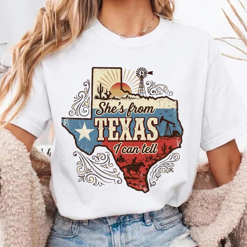 May include: White t-shirt featuring a graphic of the state of Texas with a star, the text "She's from Texas I can tell", and desert imagery. The design includes a windmill, cactus, and a cowboy riding a horse.