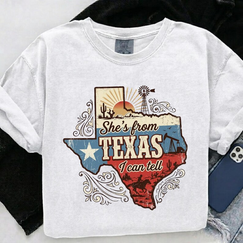 May include: White crew neck t-shirt with a graphic of the state of Texas. The graphic includes a windmill, sunset, and the text "She's from Texas I can tell" in a vintage style.