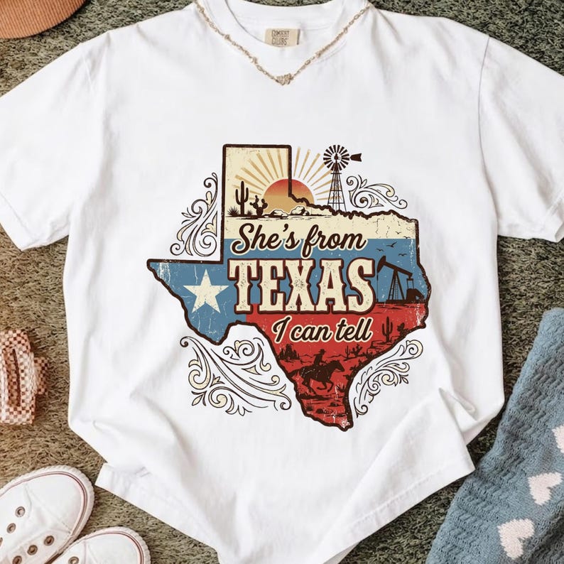 May include: White t-shirt featuring a graphic of the state of Texas with a vintage design. The design includes a star, the text "She's from Texas I can tell", a windmill, and a cowboy on a horse.