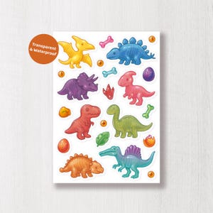 May include: A sheet of colorful dinosaur stickers. The stickers feature various dinosaurs in shades of yellow, blue, purple, red, green, and orange. The stickers also include bones, eggs, and footprints. The text "Transparent & Waterproof" is in a circle.