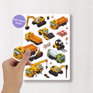 Puede incluir: Una hoja de pegatinas de vehículos de construcción con varios camiones, excavadoras y otros equipos amarillos y verdes. Las pegatinas tienen un acabado suave al tacto, como indica el texto en un círculo morado.