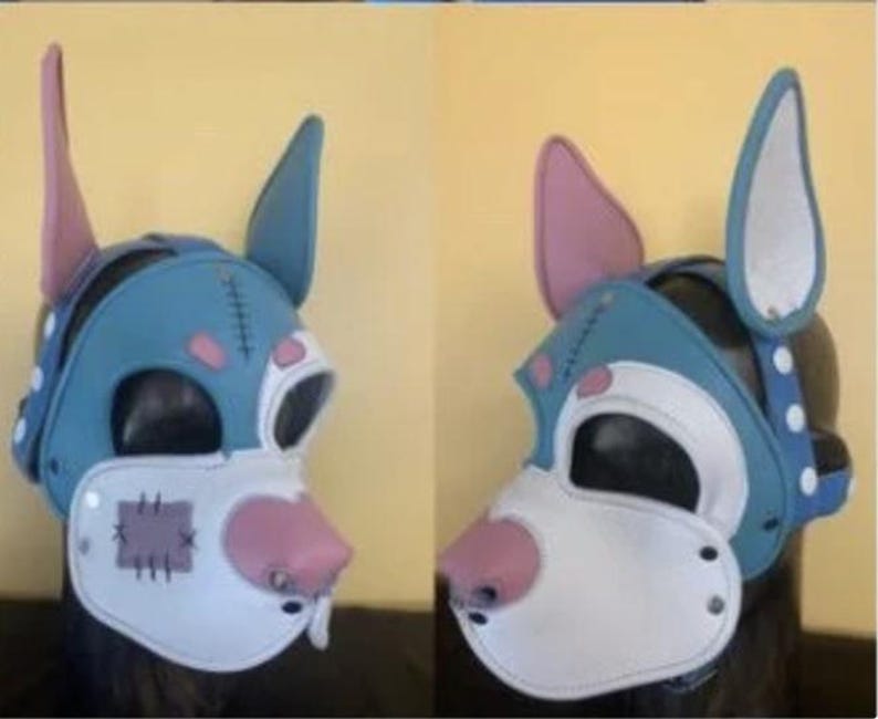 Puede incluir: Una m&aacute;scara de perro azul y blanco con detalles en rosa. La m&aacute;scara presenta orejas grandes, un hocico blanco y una nariz rosa. La m&aacute;scara tiene un dise&ntilde;o cosido y est&aacute; asegurada con remaches. La m&aacute;scara est&aacute; dise&ntilde;ada para ser usada.