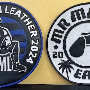 May include: Two circular patches. The left one reads "MR. MICHIGAN LEATHER 2024" around the edge, with a seated figure in the centre. The right patch says "MR. MEATUP EAST 2023" with a graphic of underwear and palm trees.