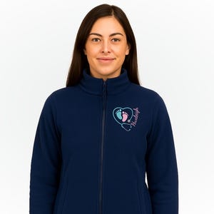 May include: Navy blue fleece jacket with a full zipper and a high collar. The jacket features a heart-shaped design with baby footprints, a stethoscope, and the name "Huxleigh" in pink and blue.