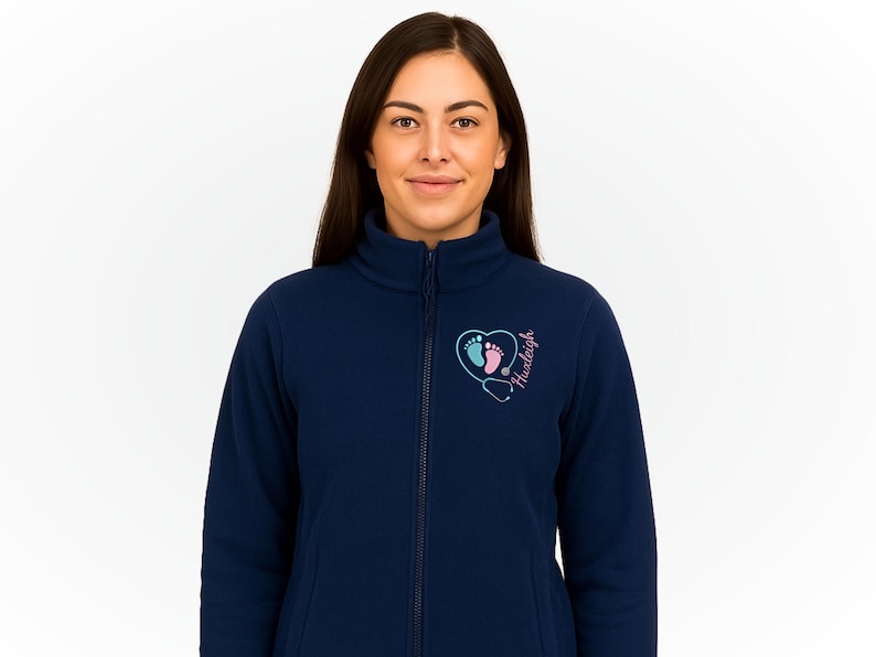 May include: Navy blue fleece jacket with a full zipper and a high collar. The jacket features a heart-shaped design with baby footprints, a stethoscope, and the name "Huxleigh" in pink and blue.