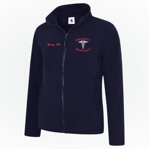May include: Navy blue fleece jacket with a zip closure and a stand-up collar. The text "Jenny, RN" is embroidered in red on the left chest, with "EMERGENCY DEPARTMENT" and a medical symbol on the right. A functional workwear item.