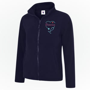 May include: Navy blue fleece jacket with a full zipper and a high collar. The jacket features a heart-shaped design with a stethoscope and the name "Breanna" embroidered in pink and teal. A comfortable and warm outerwear option.