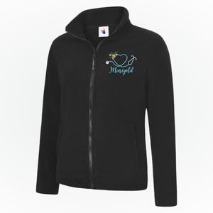 May include: Black fleece zip-up jacket with a high collar. The jacket features a stethoscope and heart design with the name "Marigold" embroidered in teal. The design includes floral accents. The jacket has two front pockets.