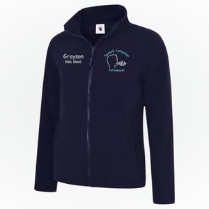 Peut inclure: Veste polaire bleu marine avec fermeture éclair intégrale et col montant. La veste présente le texte "Grayson" et "Speech Language Pathologist" avec un profil et des ondes sonores.